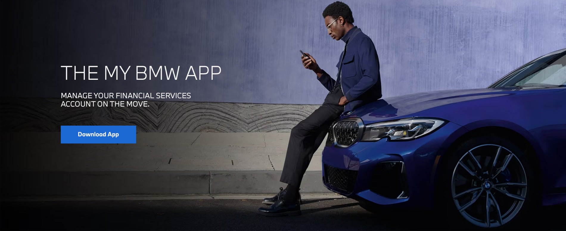 A man sits on the hood of a parked BMW while checking his phone – Link To /my-bmw-app.html
